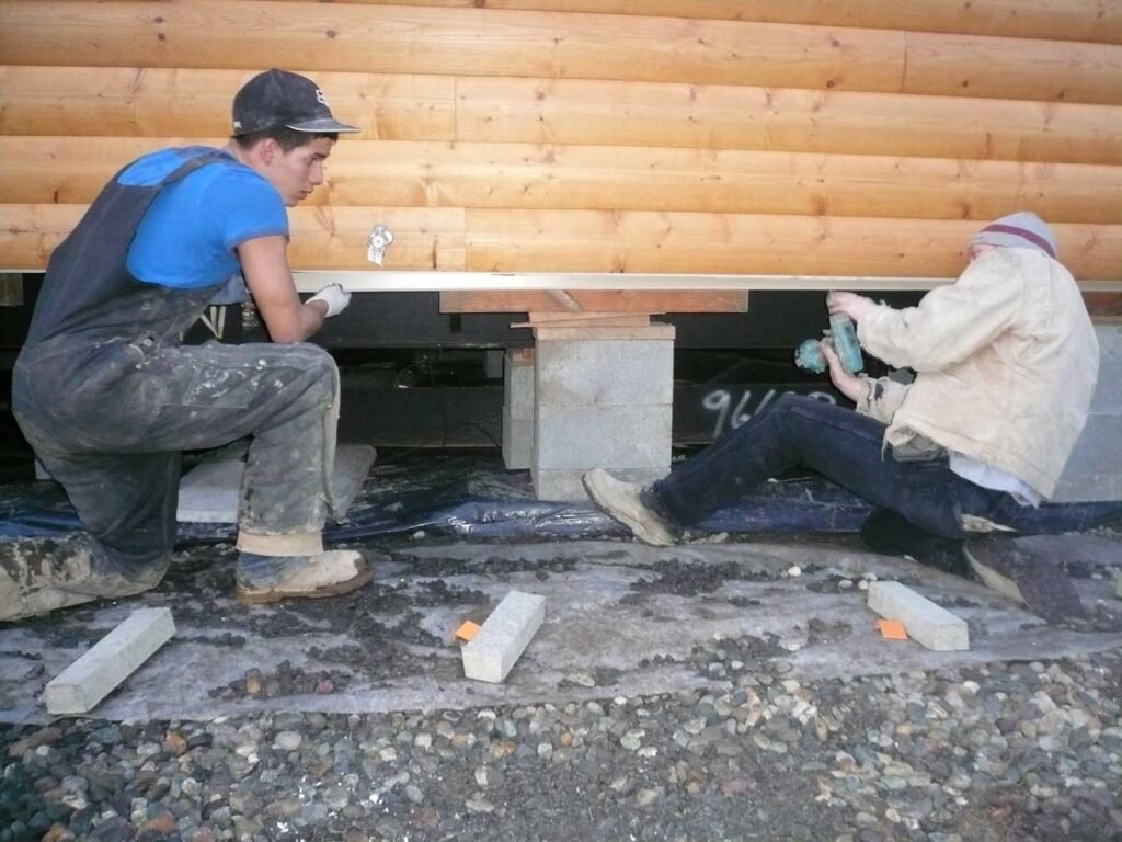 Two men working together on the foundation repair of a wooden mobile home, ensuring stability and safety.
