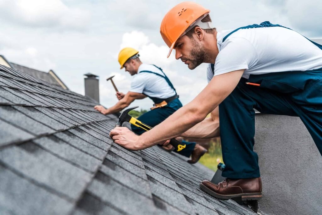Two men performing preventive maintenance on a roof, using hammers to secure shingles.