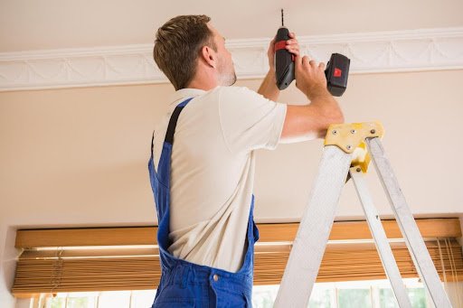 A man performs preventive maintenance by using a drill to fix a ceiling.